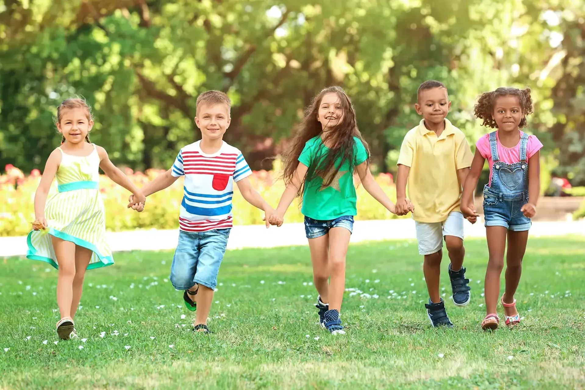 Children holding hands and walking through a park.