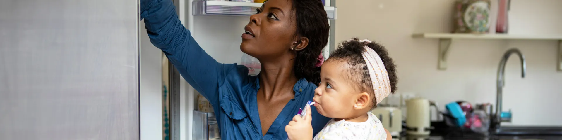 Black mother with infant daughter at open fridge.