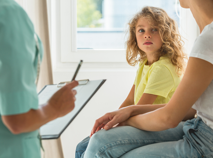 Apprehensive child sits with parents as a medical professional with a clipboard engages the family.