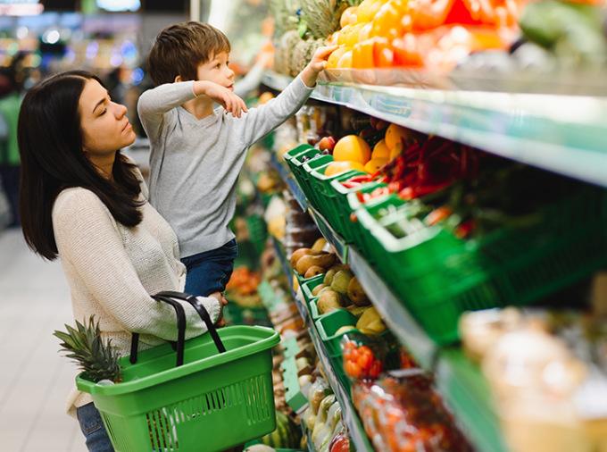 Female caretaker and child selecting produce at a grocery store.