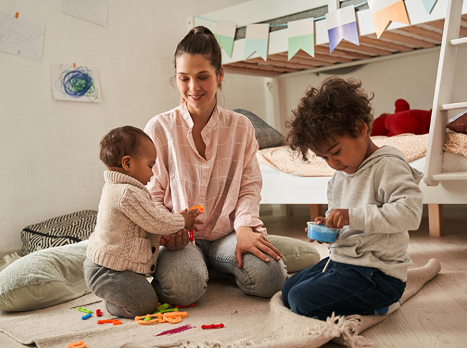 Mom on the floor of bedroom with two young children.