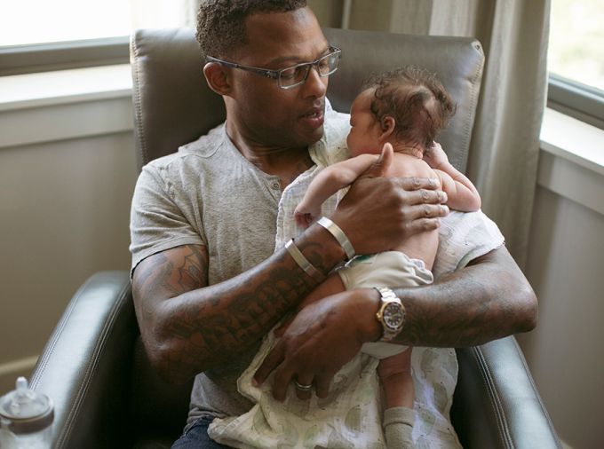 Black man wearing hospital bracelet and seated with newborn baby.