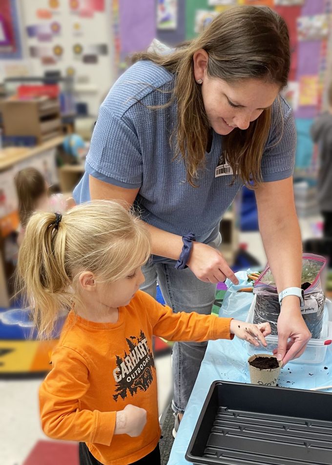 Alison Baney helping preschool student plant seeds.