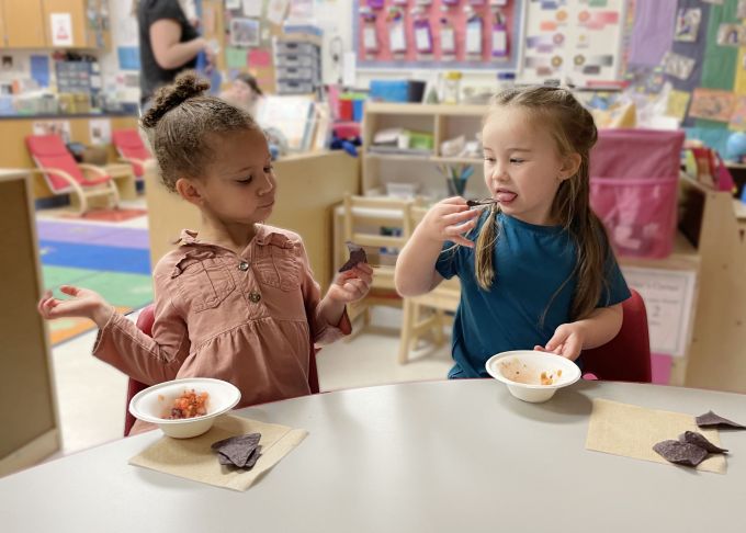 Two preschool students eating salsa.