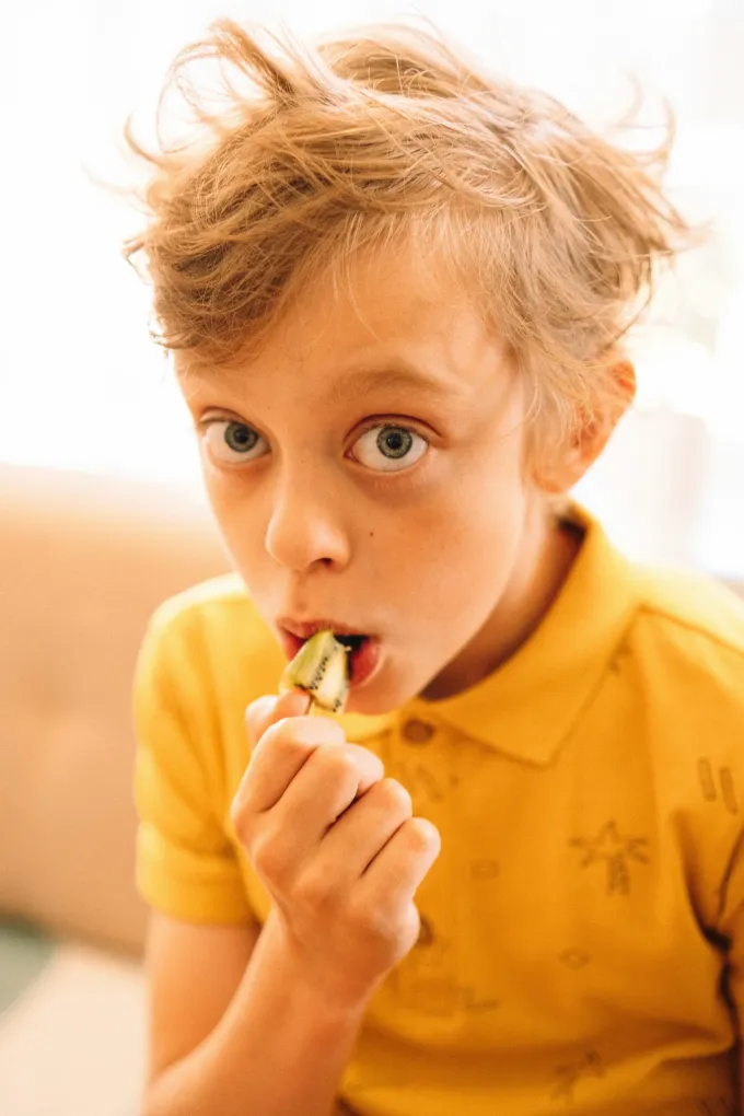 Boy in yellow shirt eats a kiwi fruit.