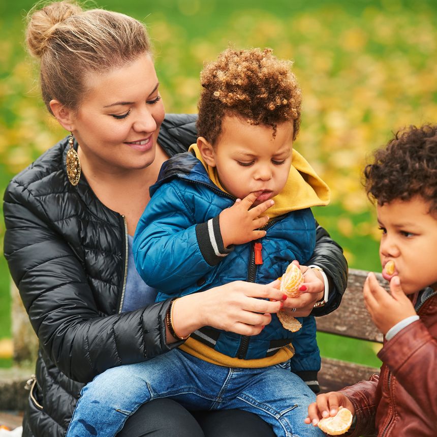 Female caregiver with two young children in a park.