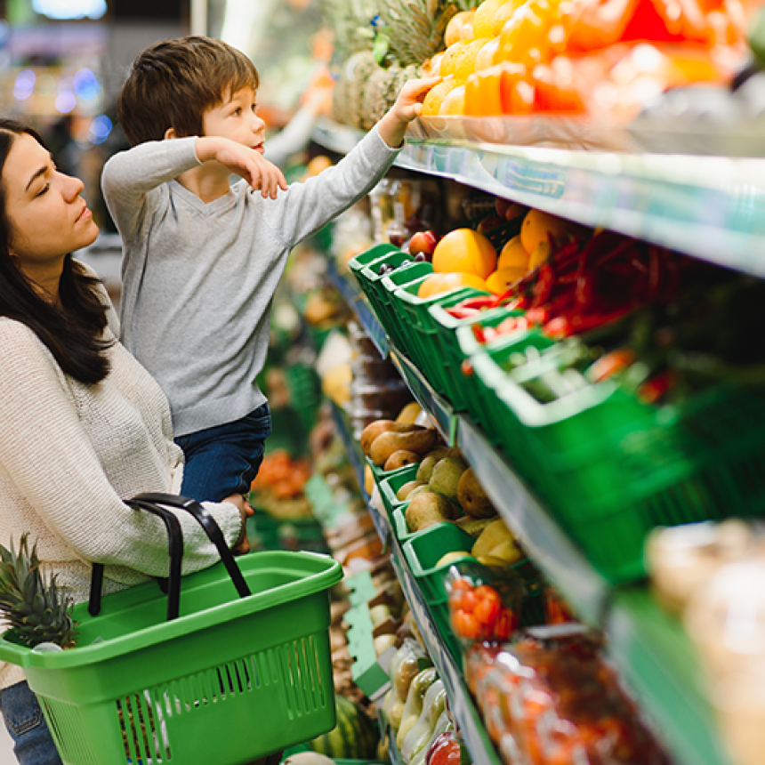 Female caretaker and child selecting produce at a grocery store.