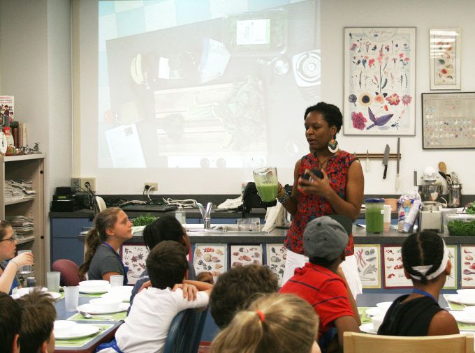 Brandi Rollins presenting green smoothies in a lab classroom of children.